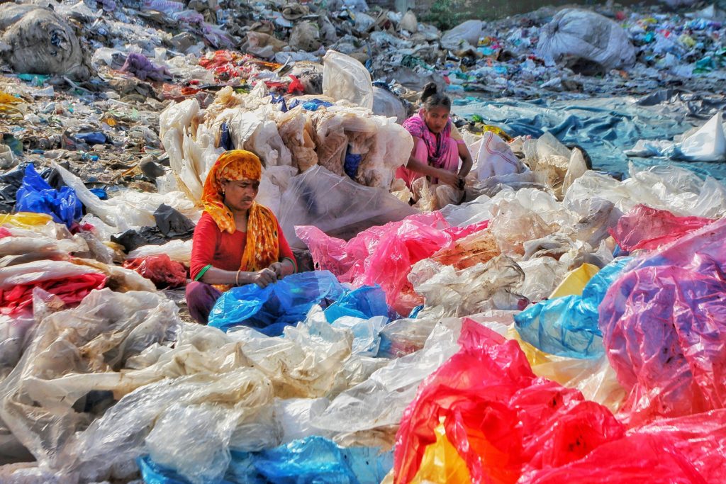 Two women sitting within a heaping pile of plastic trash.